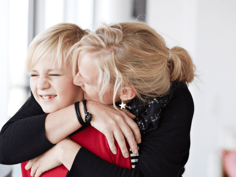 Mutter küsst ihren jungen Sohn, der peinlich wegschaut.
