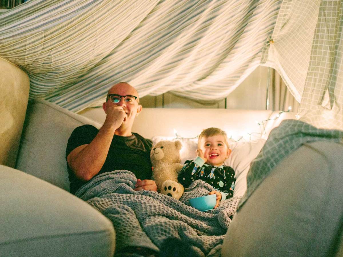 Vater und Sohn in einer selbstgebauten H&ouml;hle schauen einen Film und essen Popcorn.