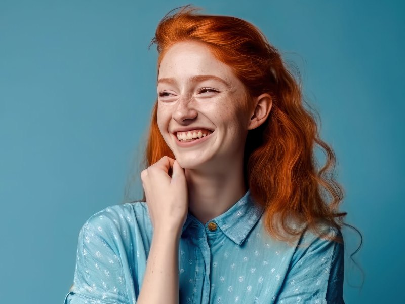 Frau mit roten Haaren steht vor einer blauen Wand und l&auml;chelt