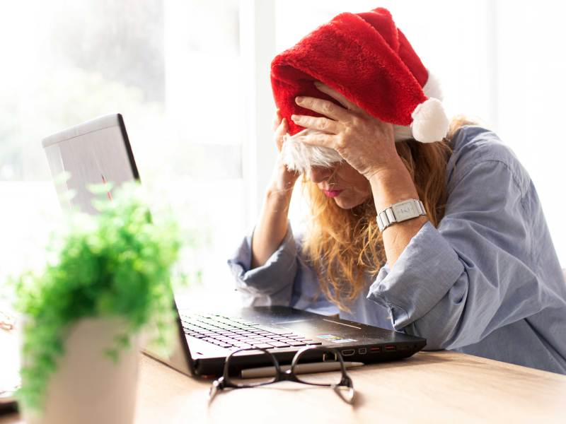 Frau mit Weihnachtsmann-M&uuml;tze sitzt verzweifelt vor ihrem Laptop und schl&auml;gt die H&auml;nde vor die Augen.