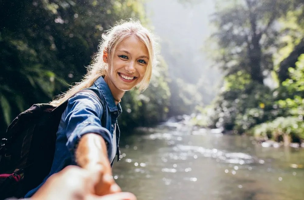 Fische Talent: Harmonie Frau an einem Fluss, die lächelnd in die Kamera blickt und ihre Hand Richtung Kamera ausstreckt