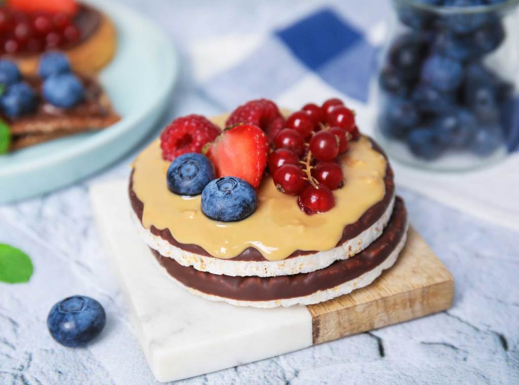 Reiswaffeln mit Schokolade, Beerenfr&uuml;chten und Erdnusscreme auf hellem Untergrund