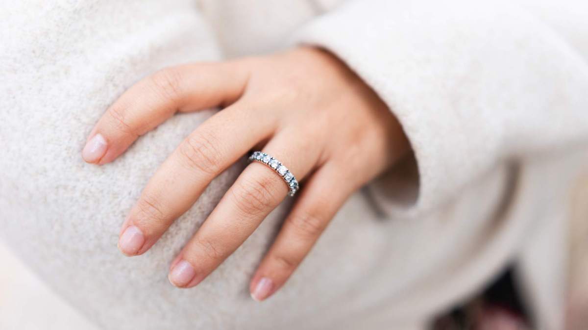 Frau mit weißem Pullover und verschränkten Armen trägt einen mit Steinen besetzten Ring.