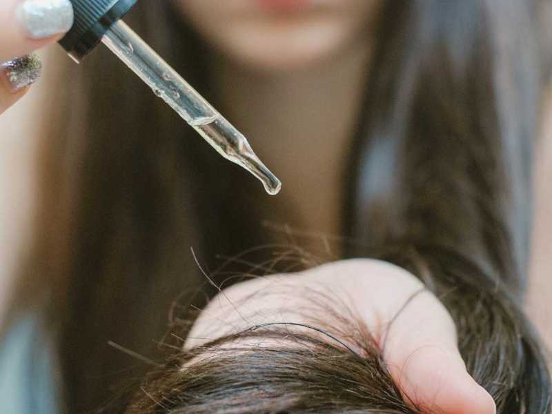 Frau trägt mit einer Pipette Öl auf die Haare auf