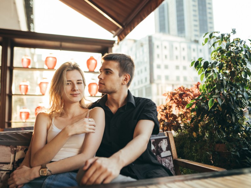 Mann und Frau in Caf&eacute;, die in der Sonne drau&szlig;en sitzen und sich umarmen