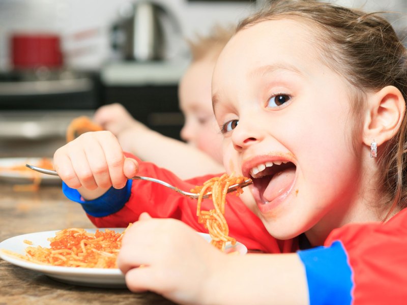 M&auml;dchen, ca. 6 Jahre alt, isst eine Portion Spaghetti mit Tomatensauce am K&uuml;chentisch.