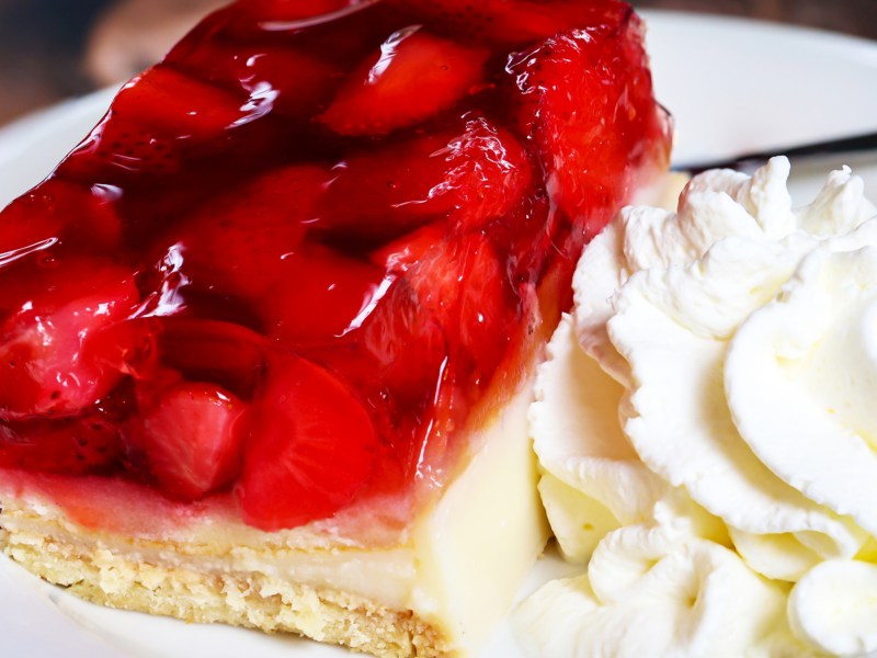 Erdbeerkuchen-Schnitte mit Sahne auf wei&szlig;em Teller.