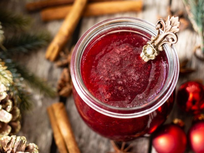 Rotes Fruchtgelee auf Holztisch mit Tannenzapfen daneben.
