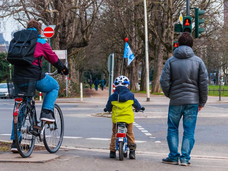Vater und ca. 4-j&auml;hriges Kind stehen auf ihren Fahrr&auml;dern sitzend an der Ampel und warten auf Gr&uuml;n.
