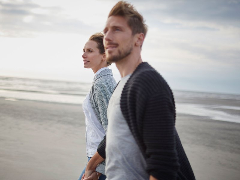 Ein Paar l&auml;uft Hand in Hand &uuml;ber den Strand.
