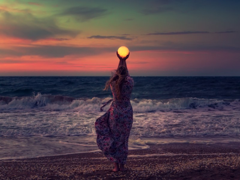 Frau am Strand, die mit ihren H&auml;nden den Mond in ihren H&auml;nden h&auml;lt