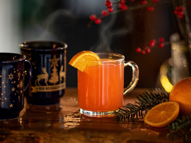 Hot Aperol auf einem Holztisch neben Glühweinbechern.