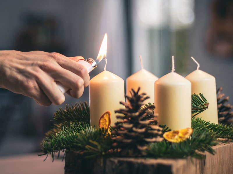 Eine Kerze auf einem Adventskranz wird mit einem Feuerzeug angez&uuml;ndet.