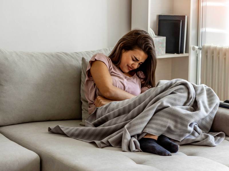 Frau mit Bauchschmerzen leigt auf Sofa