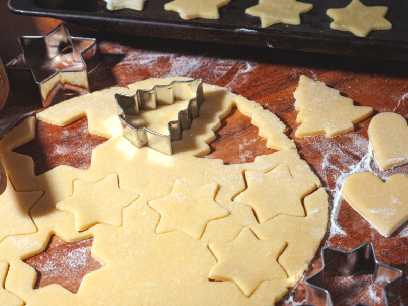 Pl&auml;tzchenteig auf Holztisch mit Ausstechformen.