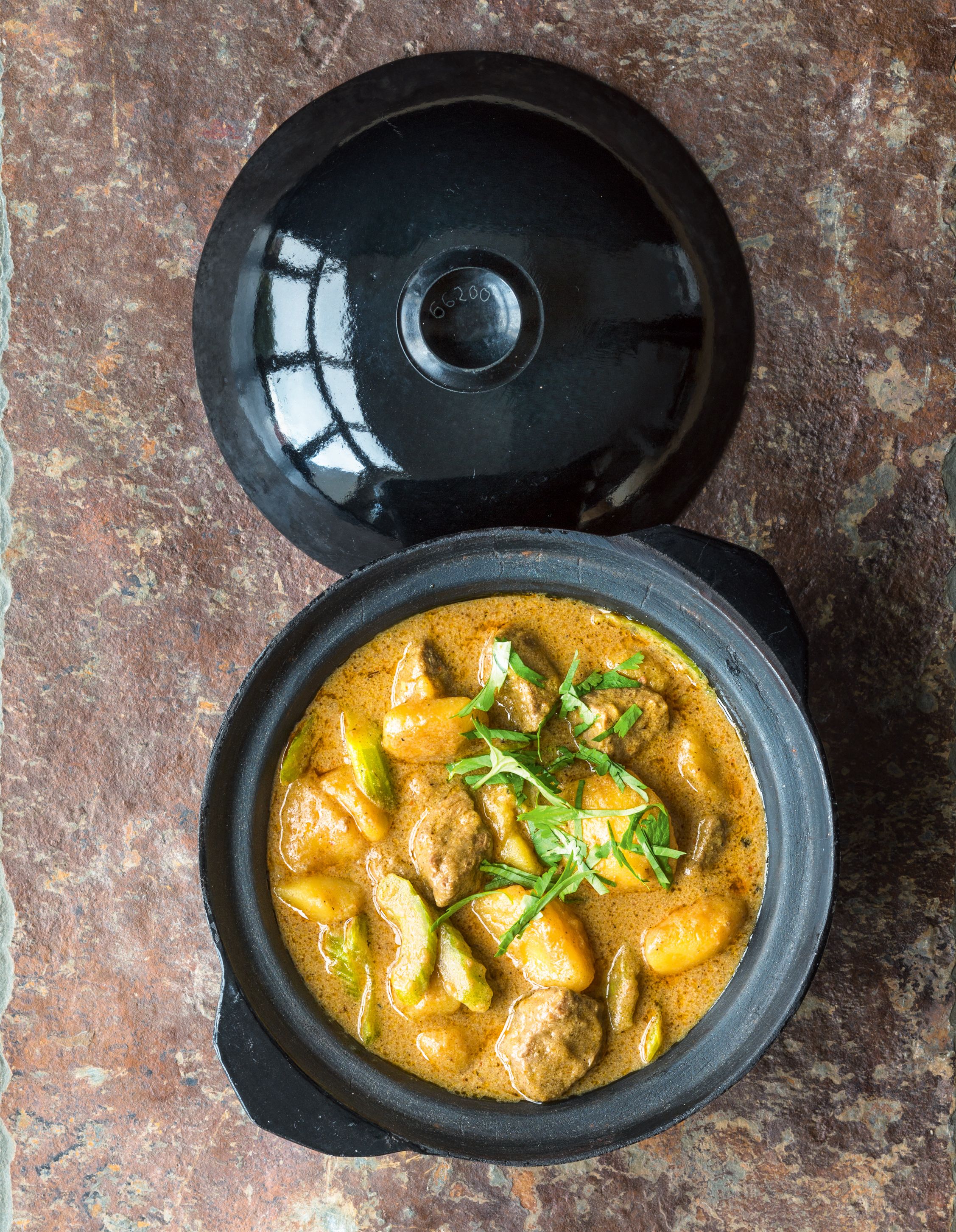 Massaman-Curry mit Rind serviert in einem kleinen schwarzen Schmortopf