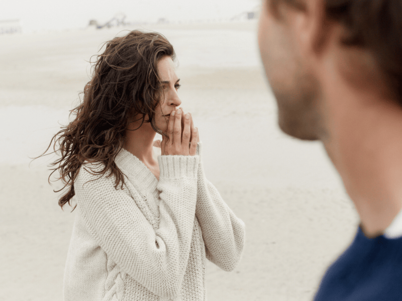 Frau steht am Strand und schaut nachdenklich in Ferne.