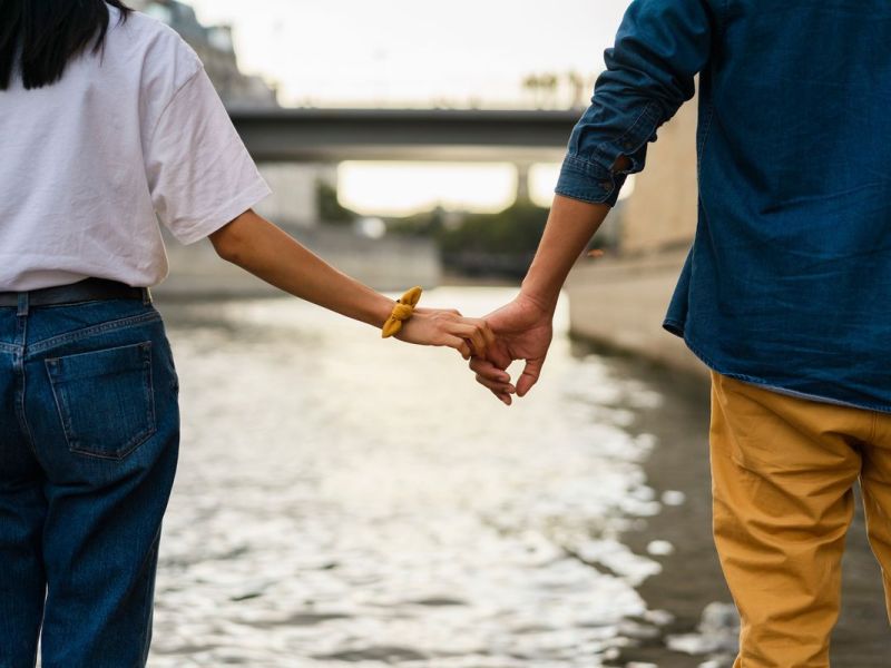 Ein paar steht Hand in Hand vor einem Fluss.