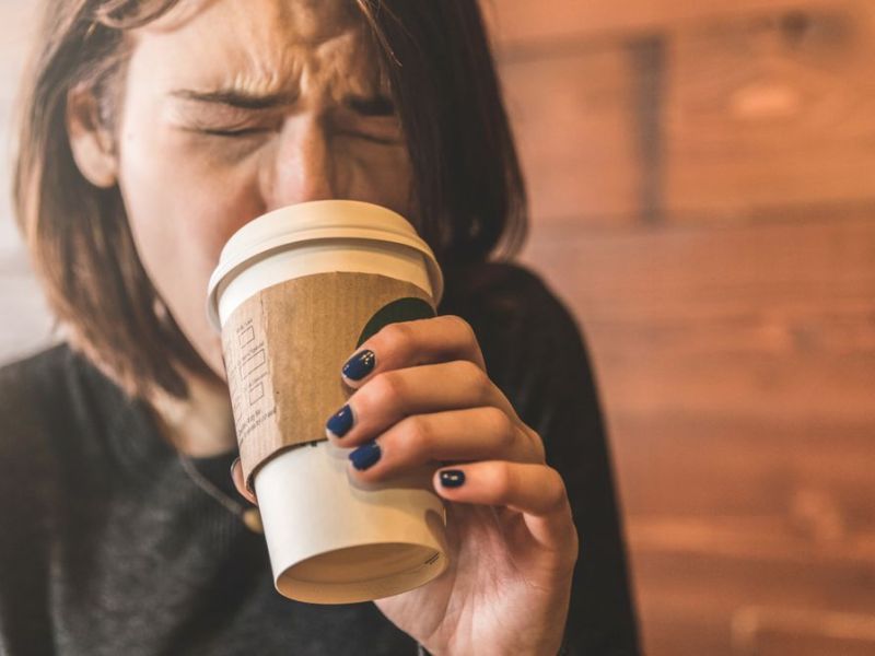 Junge Frau trinkt einen Kaffee und verbrennt sich die Zunge