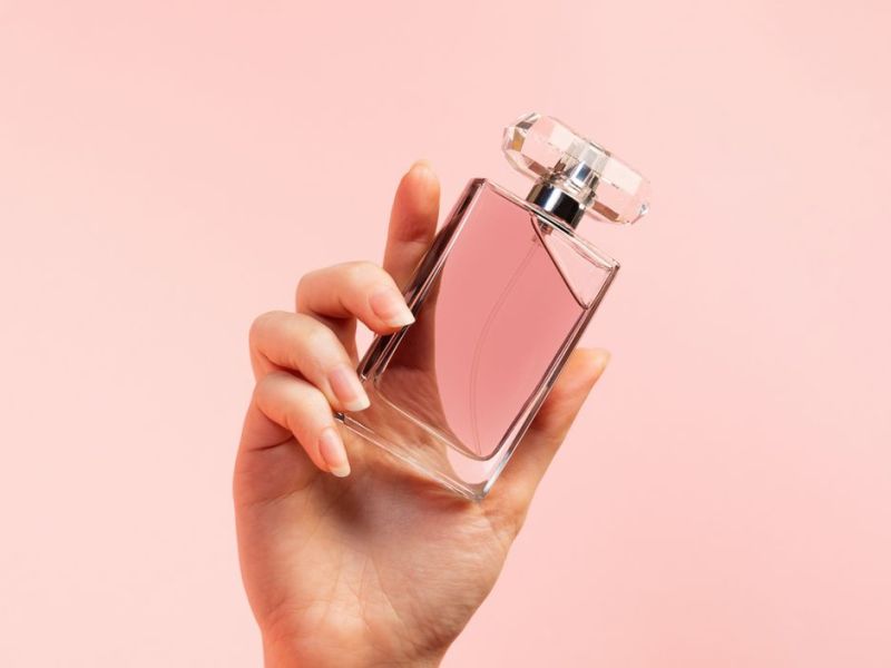 Frauenhand mit Parfum auf rosafarbenen Hintergrund
