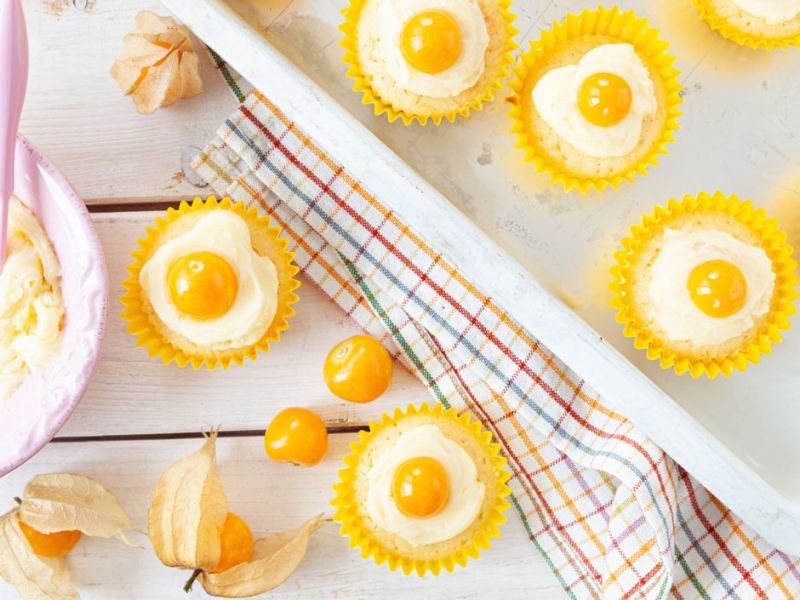 Cupcakes mit Creme und Physalis-Hälfte obendrauf auf Backblech.