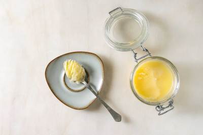 Öl, Butter und Margarine Hausgemachtes geschmolzenes Ghee, geklärte Butter in einem offenen Glasgefäß und Löffel auf einer Untertasse auf weißem Marmorhintergrund.