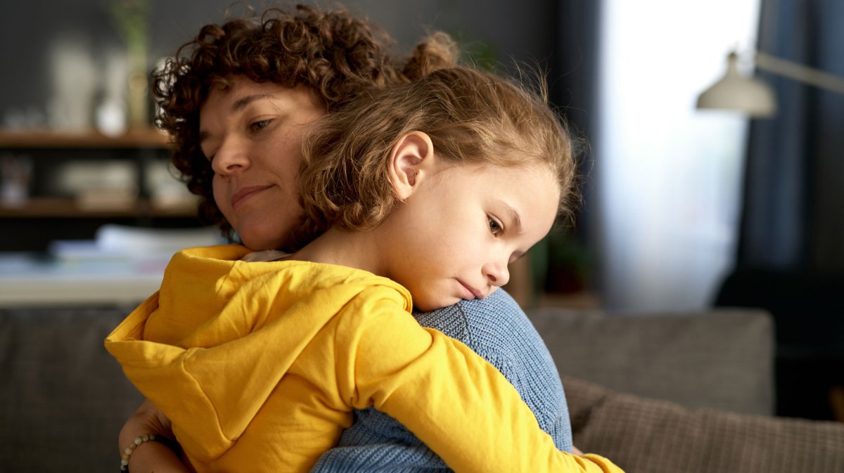 Mutter und Tochter umarmen sich. Das Mädchen, ca. 10 Jahre, sieht traurig und enttäuscht aus.
