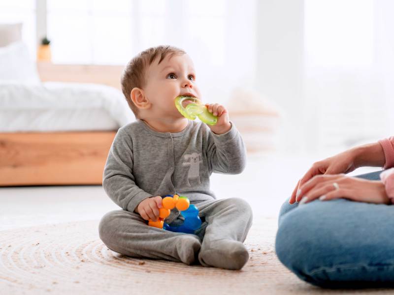 Baby sitzt auf dem Boden und kaut auf einem Bei&szlig;ring herum.