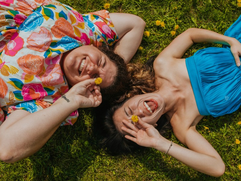 Frau und Mann auf einer Wiese, die lachen und nach oben in die Kamera schauen.