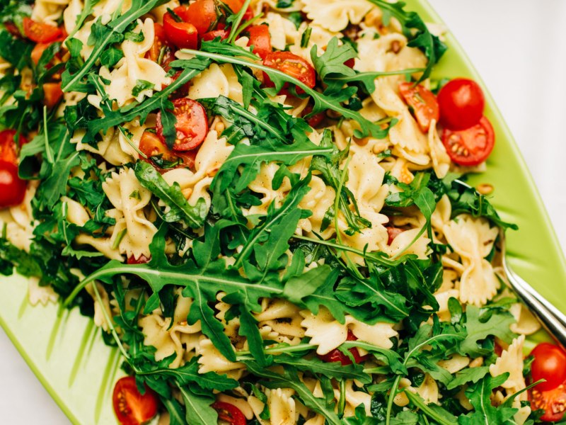 Nudelsalat mit Farfalle, Rucola und Tomaten in einer gr&uuml;nen Serviersch&uuml;ssel.