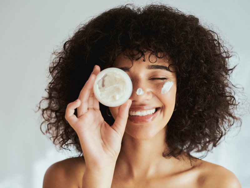 Anti-Aging-Creme-test: Frau trägt Creme auf Gesicht auf und lacht