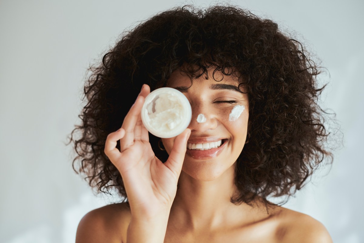 Anti-Aging-Creme-test: Frau trägt Creme auf Gesicht auf und lacht