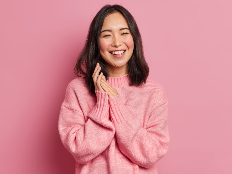 Junge asiatische Frau in Rosa gekleidet l&auml;chelt in Kamera.