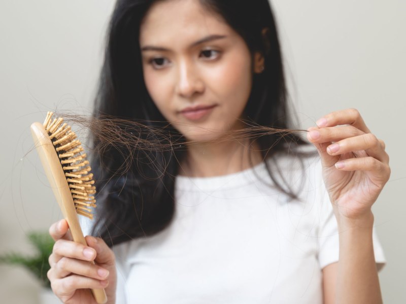 Frau, die Haarb&uuml;schel aus der B&uuml;rste zieht.