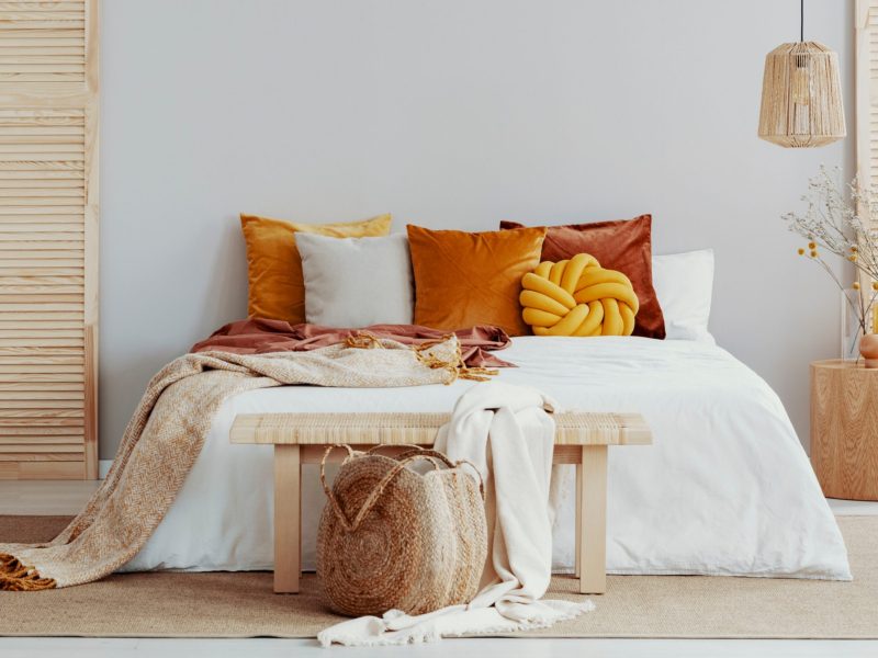 Bett dekoriert mit Kissen, einer Tagesdecke und einer Bank am Fußende