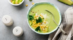 Eine wei&szlig;e Schale mit der hellgr&uuml;nen Suppe auf einem grauen Tisch. Alles direkt von oben fotografiert.