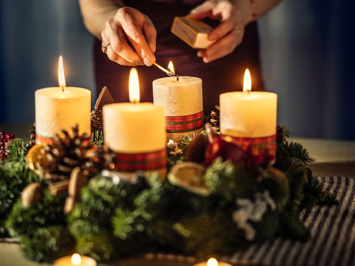 Eine Frau z&uuml;ndet die vierte Kerze eines Adventskalenders an.