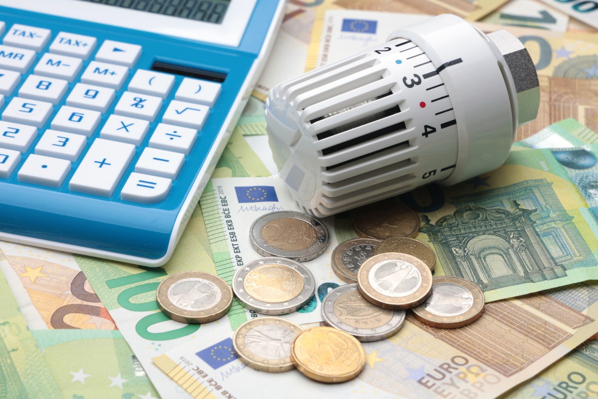 Geldscheine, Münzen, Taschenrechner und Heizungsthermostat auf Tisch