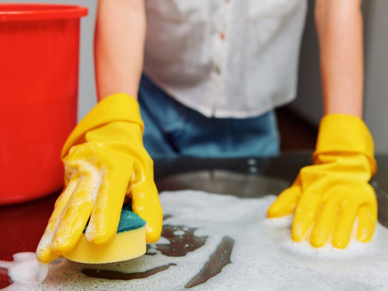 Frau putzt mit Handschuhen und Schwamm eine Oberfl&auml;che