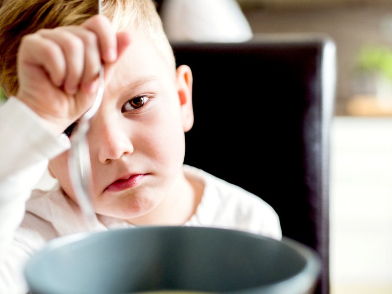 Nahaufnahme eines Jungen, der am Tisch sitzt und seine Suppe vor ihm nicht essen m&ouml;chte.
