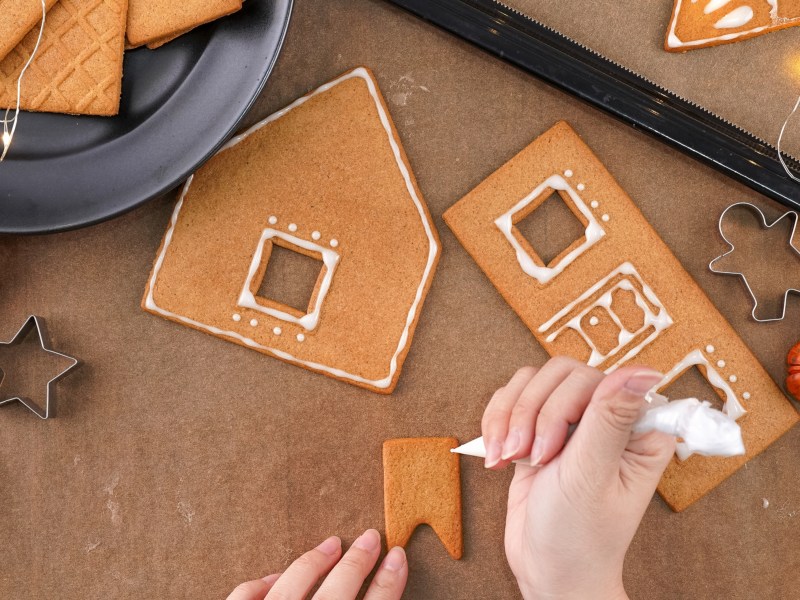 Eine Hand dekoriert Lebkuchen f&uuml;r ein Lebkuchenhaus.