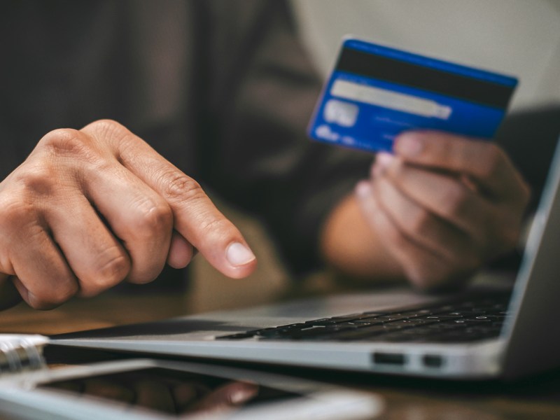 Frau h&auml;lt Bankkarte in der Hand und tippt auf dem Laptop.