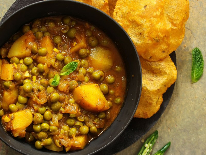 Kartoffelcurry in einer schwarzen Schale mit Brot angerichtet