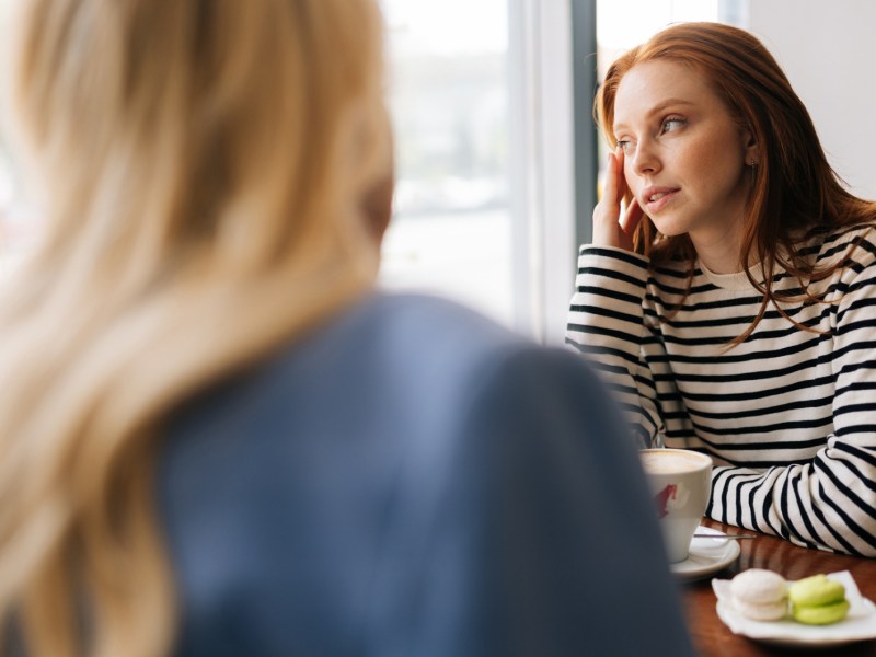 Zwei Frauen in einem Caf&eacute;, w&auml;hrend die eine leicht vertr&auml;umt zur Seite aus dem Fenster schaut