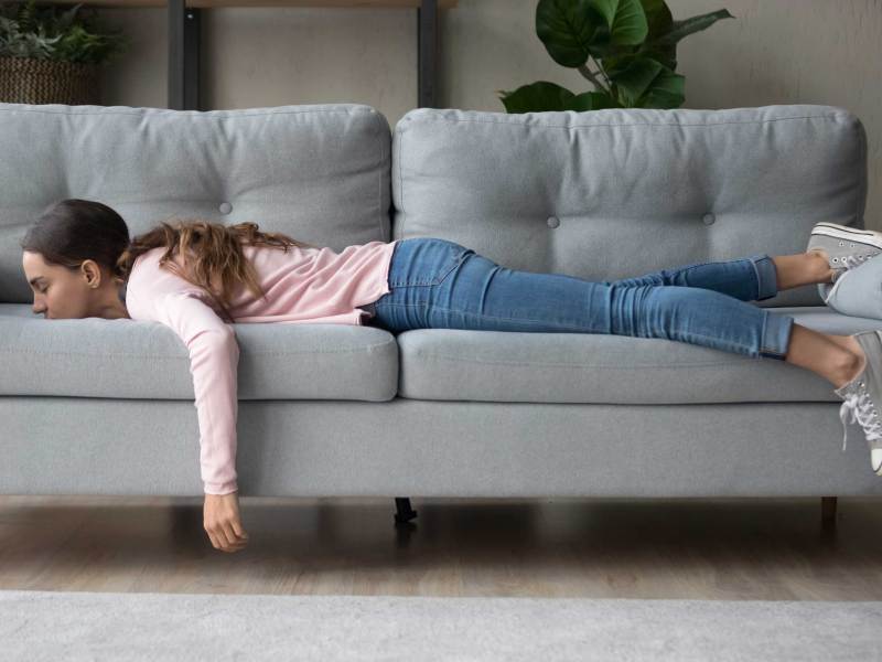 Junge Frau liegt mit dem Gesicht im Sofa vergraben und f&uuml;hlt sich m&uuml;de