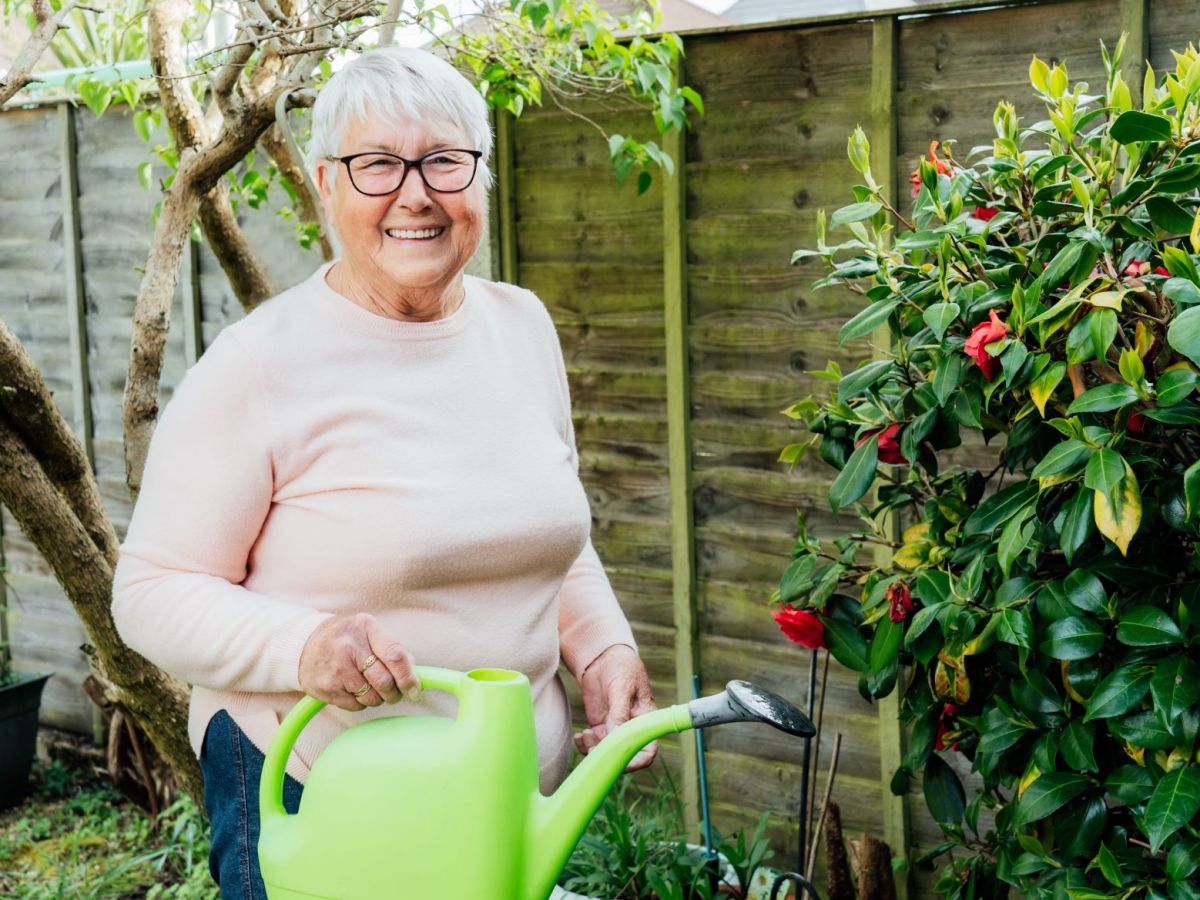 &Auml;ltere Frau im Garten mit gr&uuml;ner Gie&szlig;kanne