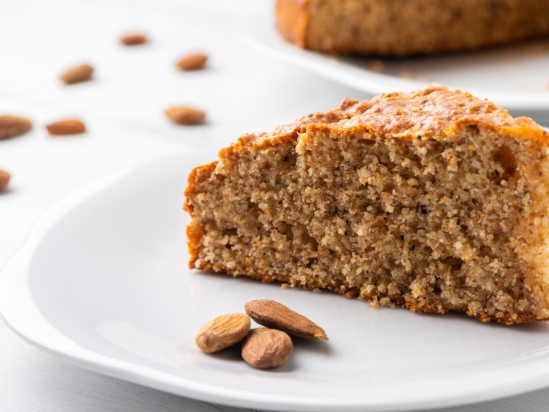 Ein St&uuml;ck dunkler Mandelkuchen auf einem wei&szlig;en Teller.