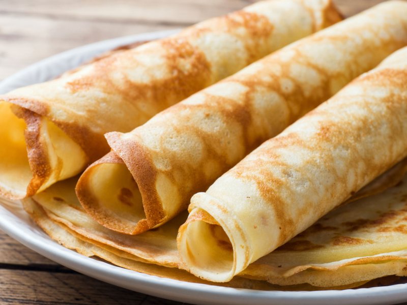 D&uuml;nne Crepe-Pfannkuchen auf einem Teller gestapelt, die obersten sind gerollt.