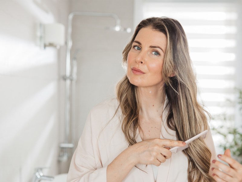 Frau, die sich ihre langen Haare k&auml;mmt.