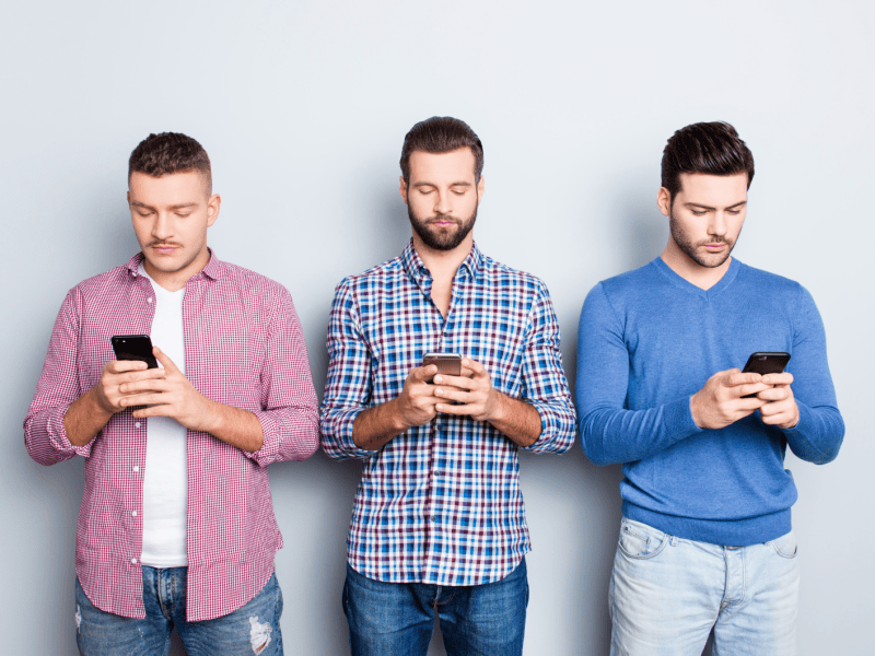 Drei M&auml;nner mit Handy in der Hand, die auf das Display schauen und tippen.